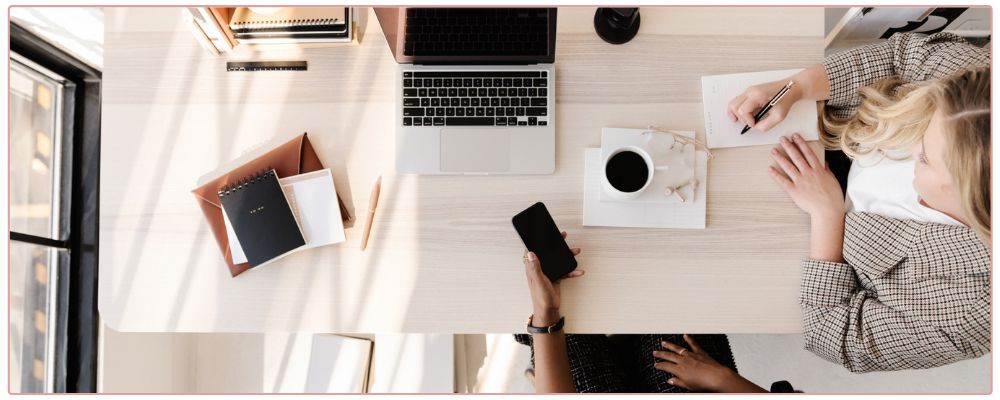 woman working on her pink laptop with her cell phone on her desk
